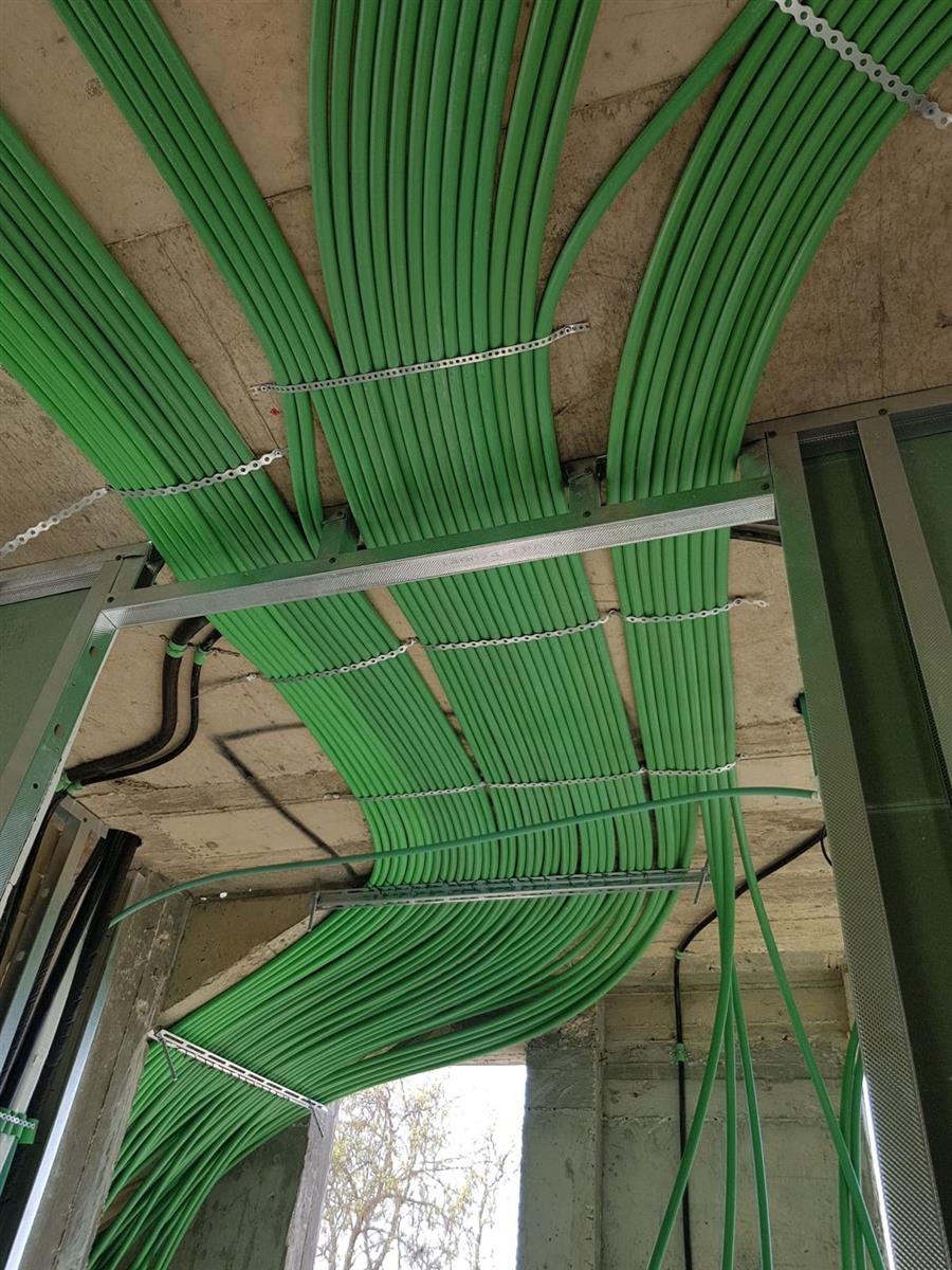 עשרות צינורות חשמל ירוקים נפרשים במניפה על תקרת בטון, מחוזקים בתפסניות במרווחים אחידים