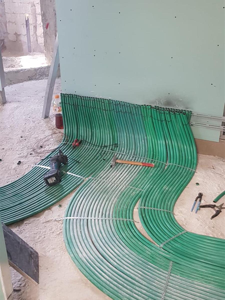 צינורות ירוקים מעוקלים בקשת אחידה על הרצפה, בשלב העבודה, לצד כלי העבודה