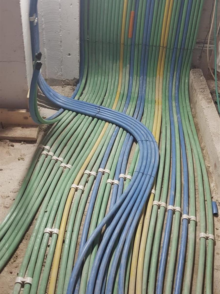 מסלול צינורות על הרצפה לפני יציקת מדה, מהודק בתפסניות, עם צינורות כחולים שחוצים אותו